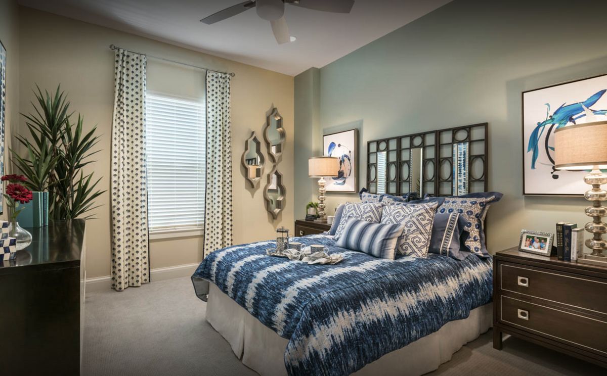 A cozy bedroom featuring blue and white bedding, decorative pillows, a stylish table lamp, and wall art accents.