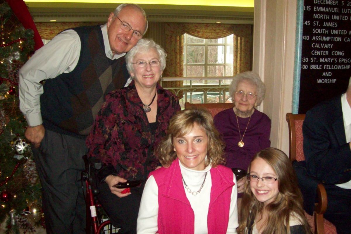 A multi-generational family gathering indoors, captured in a group photo with smiles.
