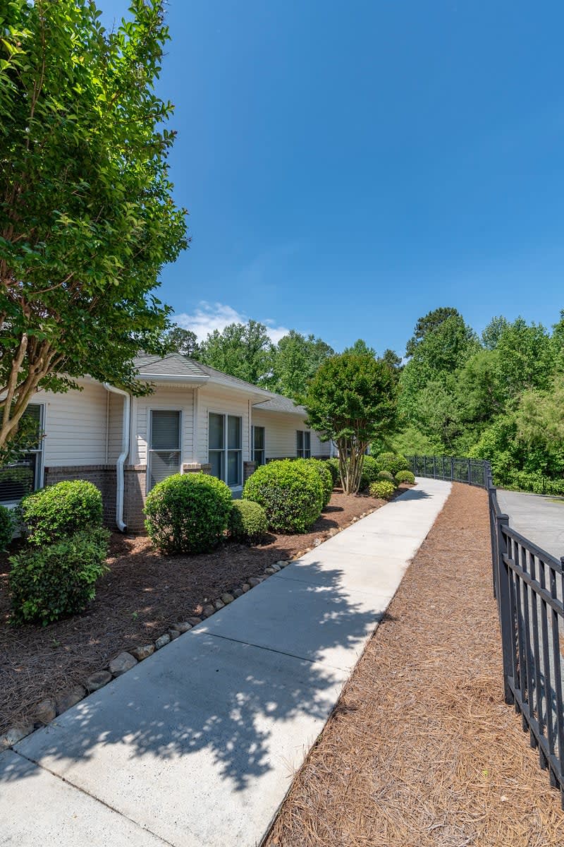 A quaint residential property with a well-maintained sidewalk and lush landscaping on a sunny day.