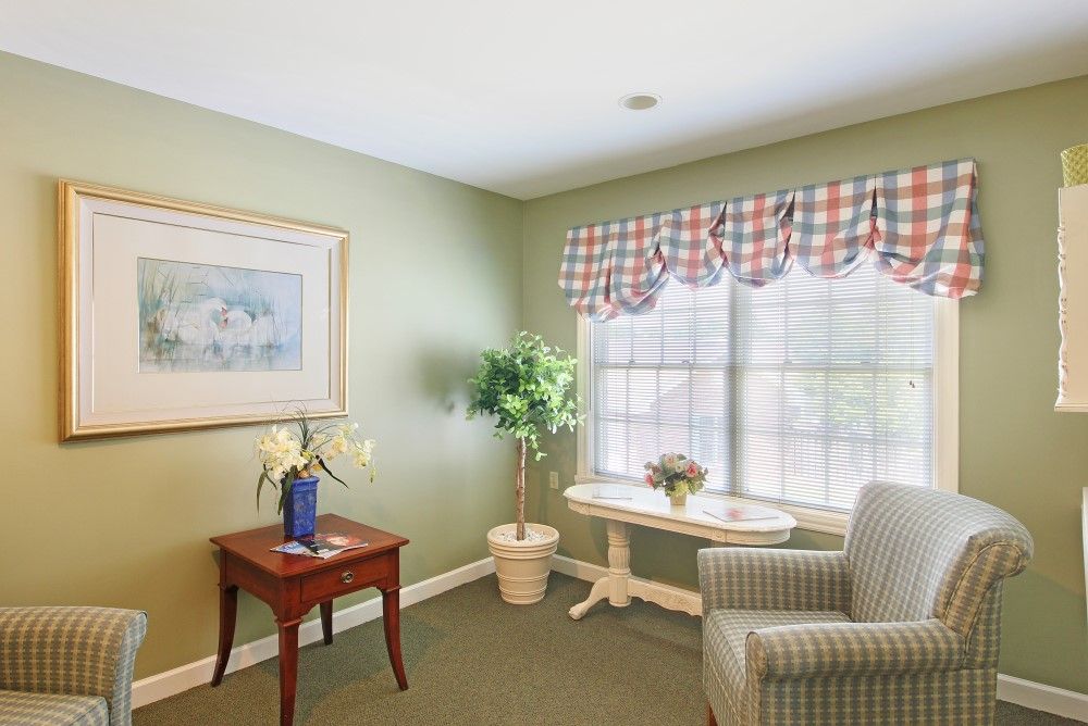 A cozy living room with a table, chair, and large window featuring patterned curtains.
