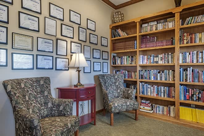 A cozy reading corner with bookshelves, armchairs, and framed certificates on the wall.