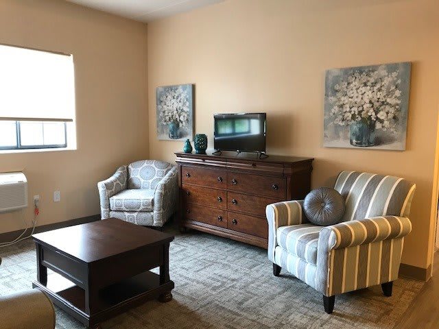 A cozy living room with armchairs, a coffee table, a cabinet with a television, and decorative paintings.