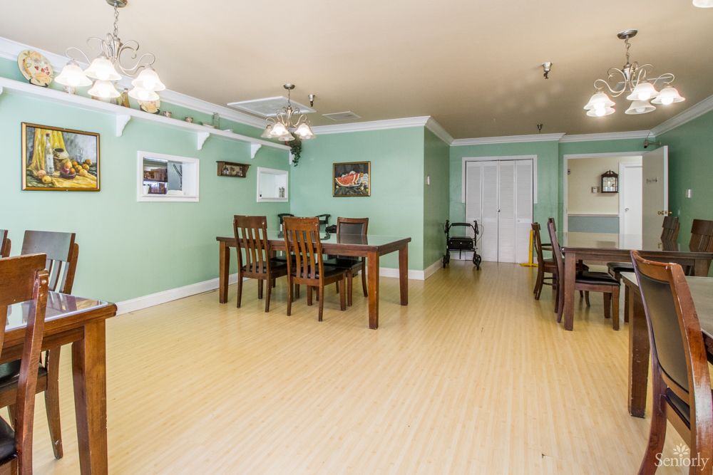 A spacious dining room with wooden furniture and green walls, featuring ceiling fans and a light wooden floor.