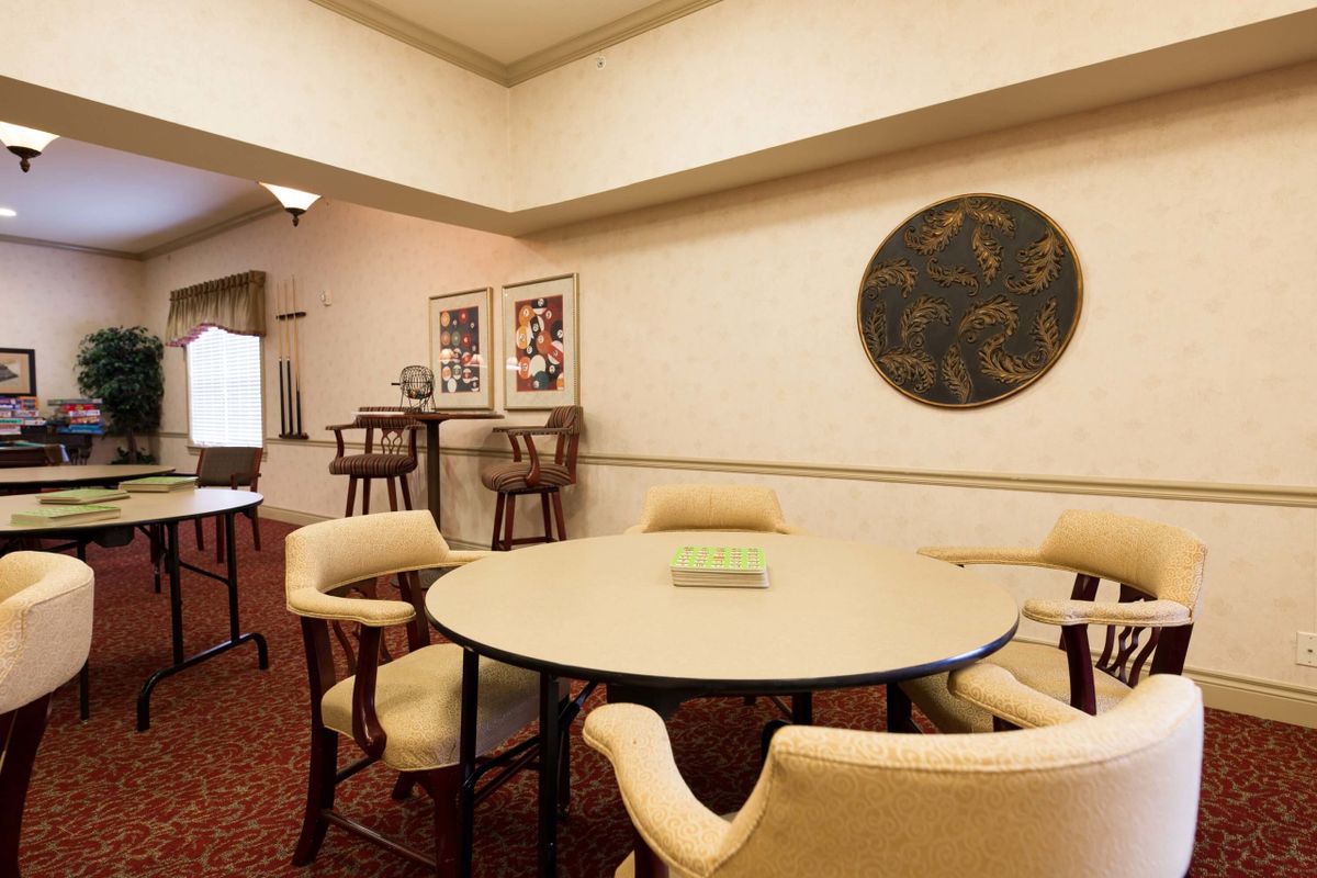 A cozy meeting room with a round table and chairs, featuring wall art and a carpeted floor.
