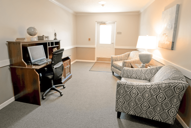A cozy office space with a computer desk, chair, and patterned armchairs.