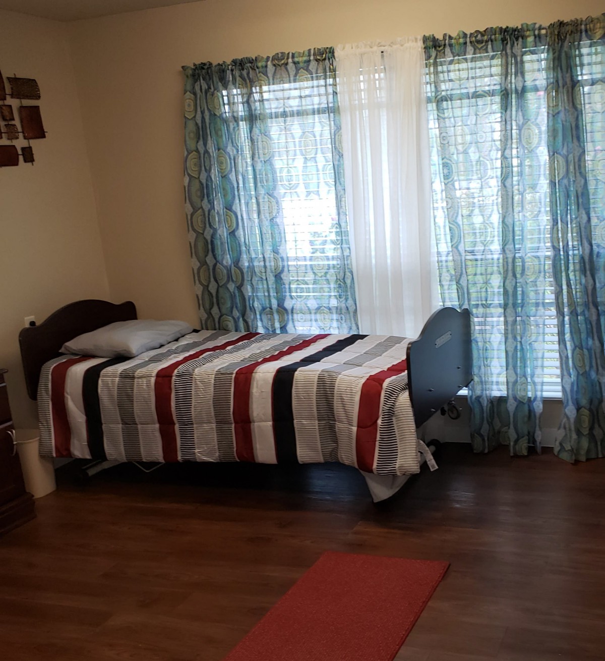 A cozy bedroom with a single bed featuring striped bedding, a desk by the window, and soft blue curtains.