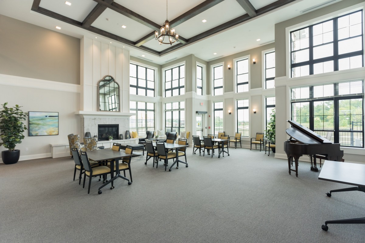 A spacious and elegant dining area with high ceilings, large windows, a chandelier, and a grand piano.