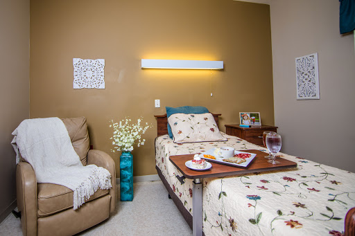 A cozy and thoughtfully decorated bedroom featuring a comfortable chair, a neatly made bed, and personal touches like flowers and books.