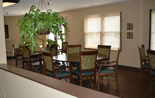 A cozy dining room featuring a large wooden table, comfortable patterned chairs, and a hanging plant near the window.