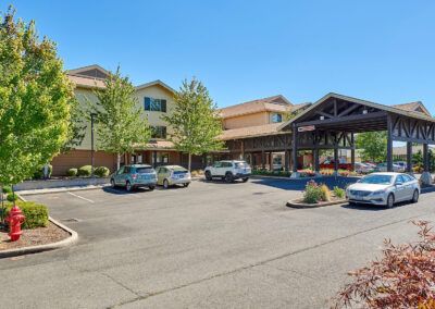 A large hotel building with a parking lot in front, surrounded by trees on a sunny day.