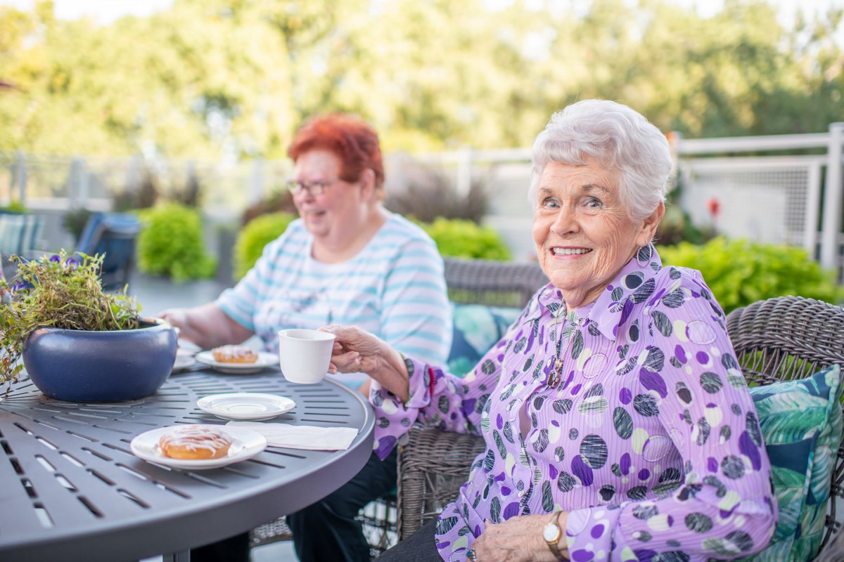 Two elderly women enjoying tea and conversation outdoors.