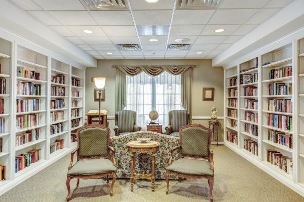A cozy library reading room with bookshelves, elegant chairs, and a central table.