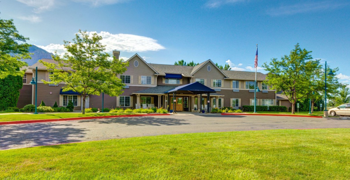 A large building with a welcoming entrance surrounded by greenery on a sunny day.