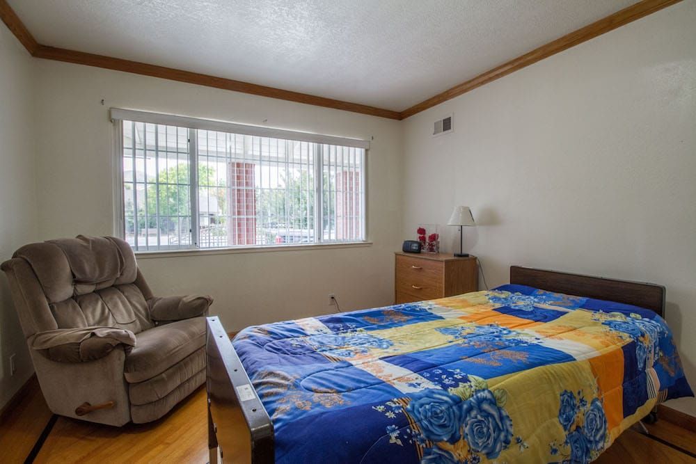 A cozy bedroom with a bed, chair, and large window allowing natural light.