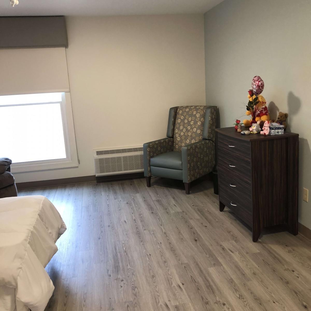 A neatly arranged bedroom with a chair, dresser, and window.