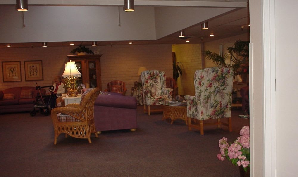 A cozy living room with various seating options, including sofas and floral-patterned chairs, illuminated by lamps.