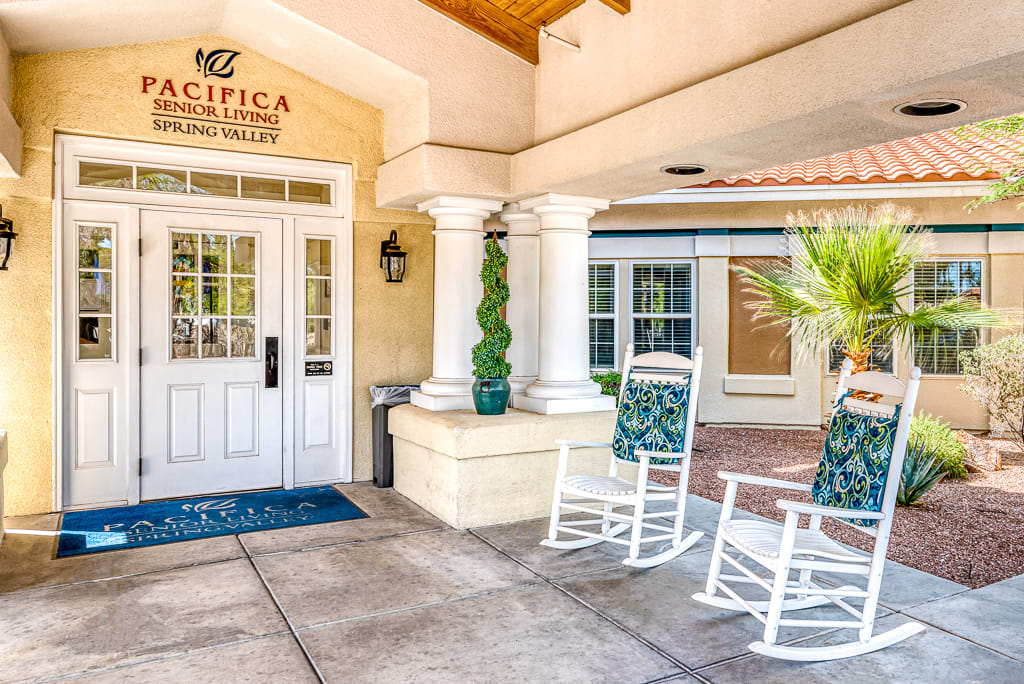 Entrance of a building with rocking chairs and decorative columns.