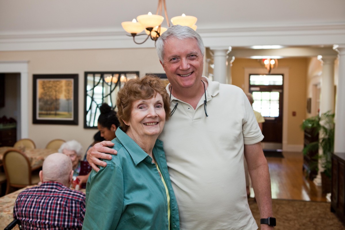 An elderly couple smiling and posing together at a family gathering indoors.