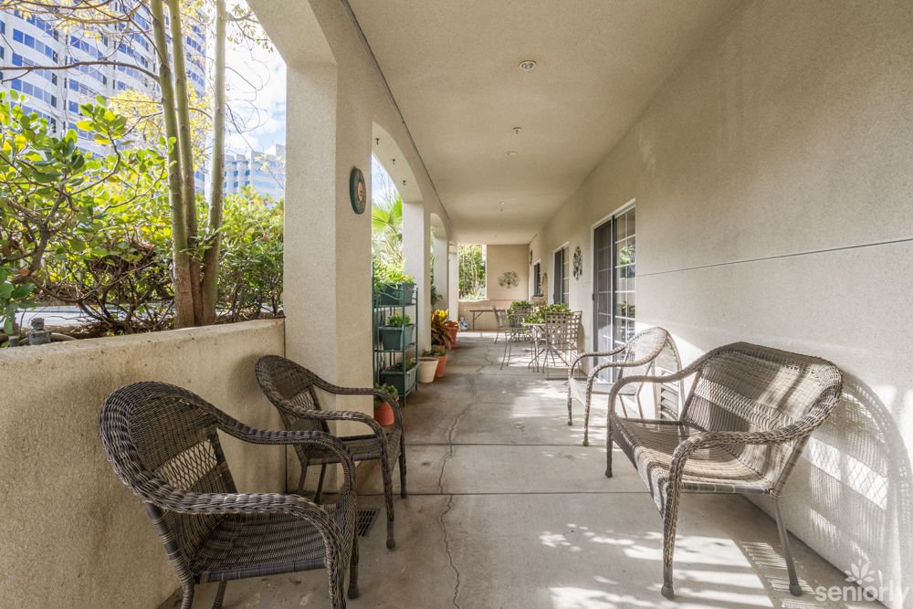 A peaceful outdoor patio with wicker chairs and greenery along a corridor.