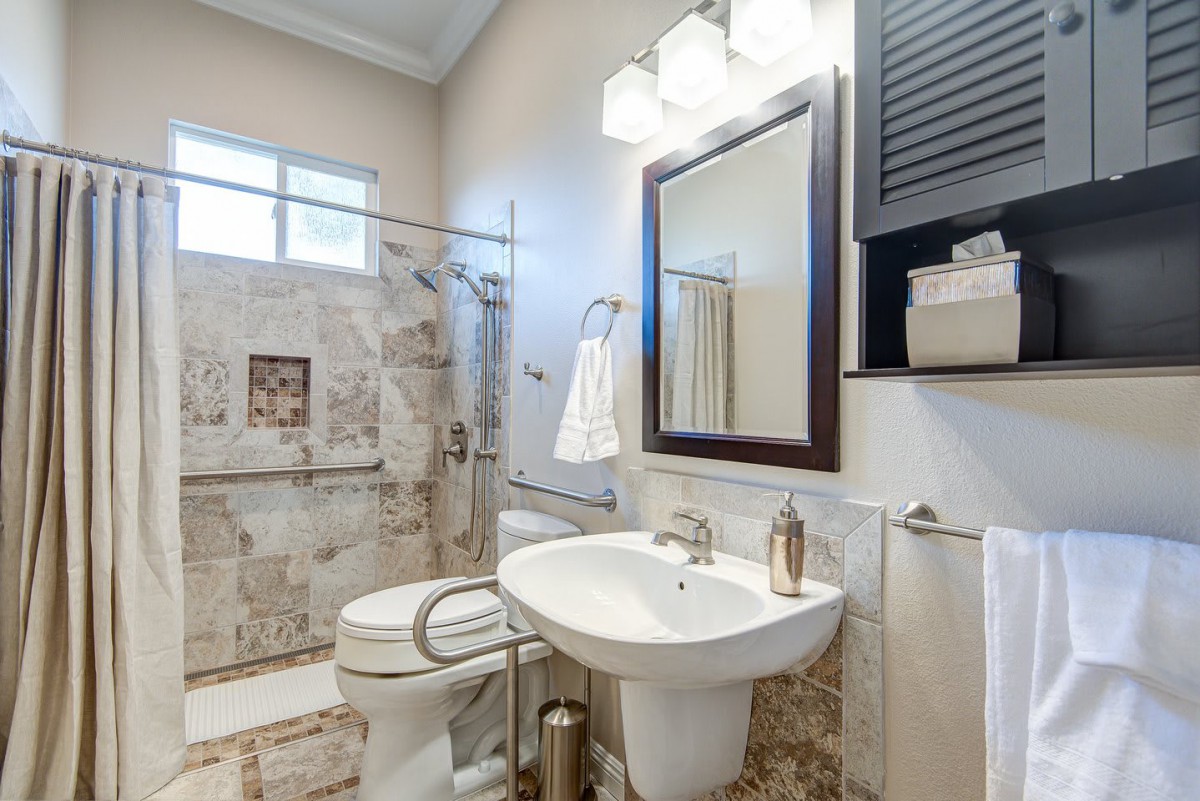 A modern bathroom featuring a tiled shower, pedestal sink, and large mirror.