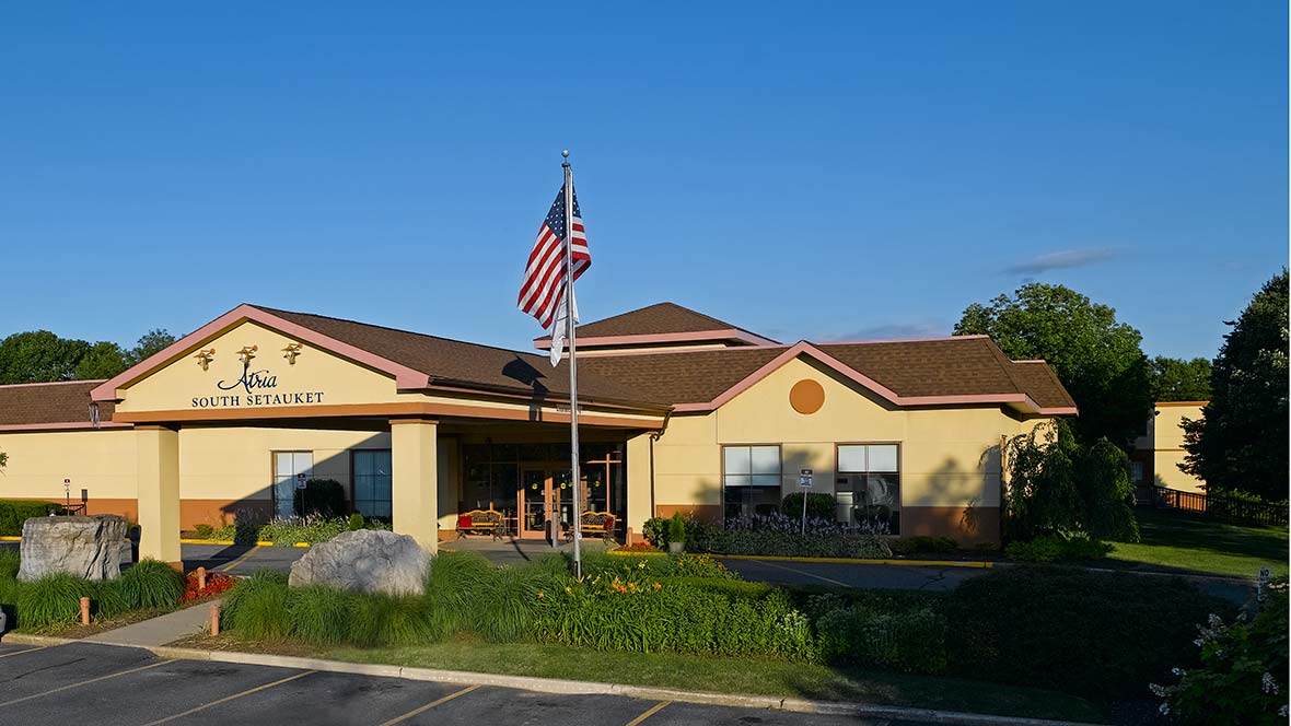 A building with an American flag flying in front, surrounded by greenery on a sunny day.