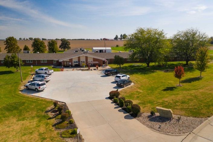 Aerial view of a building with a circular driveway and parking lot surrounded by landscaped greenery on a sunny day.