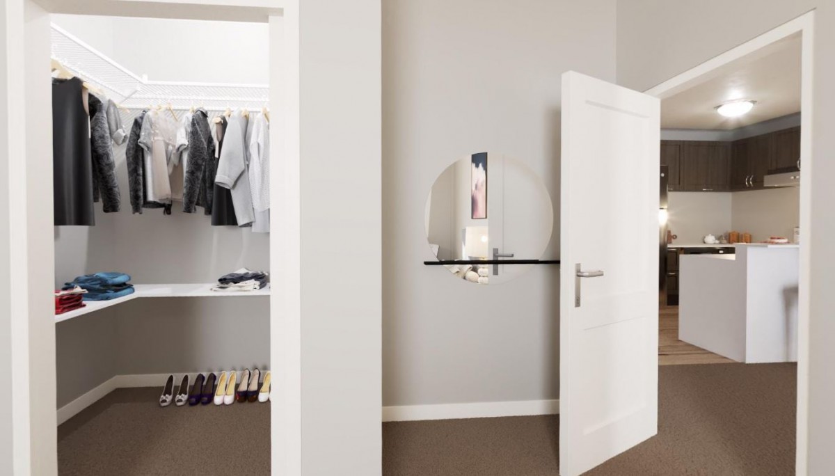 A minimalist room featuring an open closet with neatly hung clothes and a circular mirror on the wall.