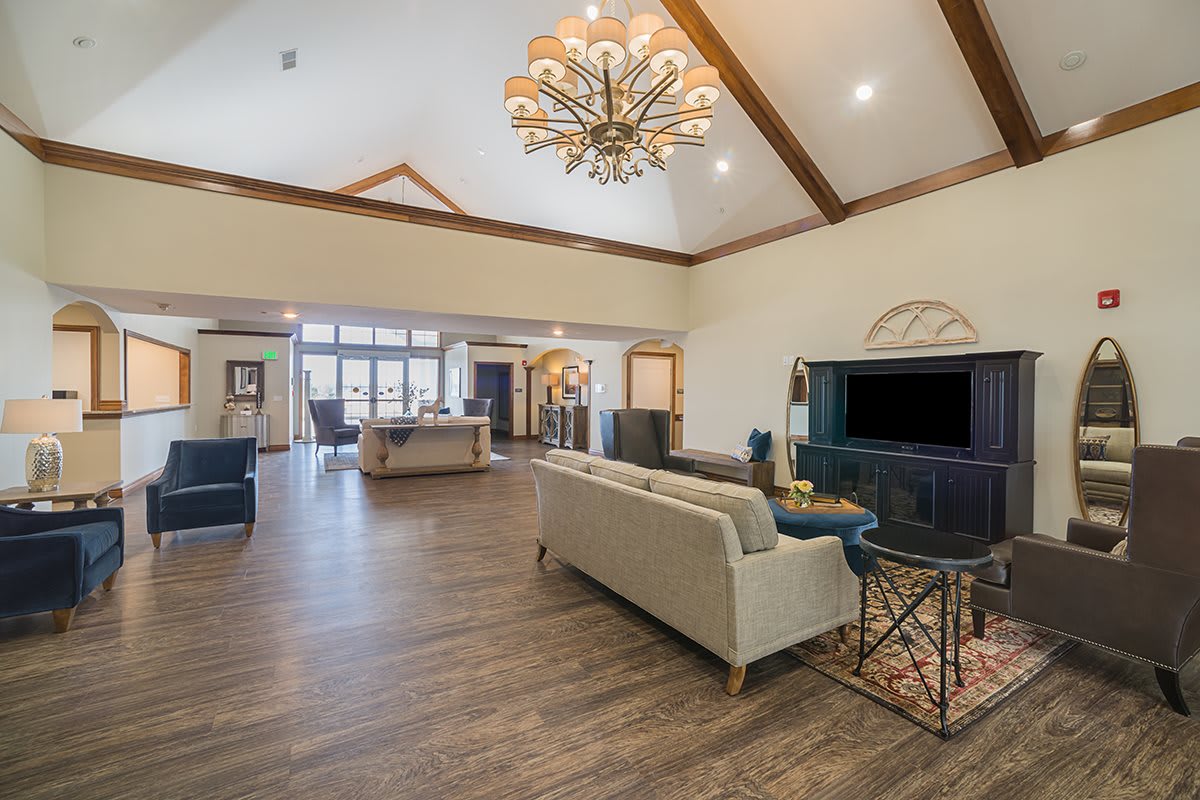 A spacious living room with a high ceiling, featuring a sofa, television, and chandelier on a wooden floor.