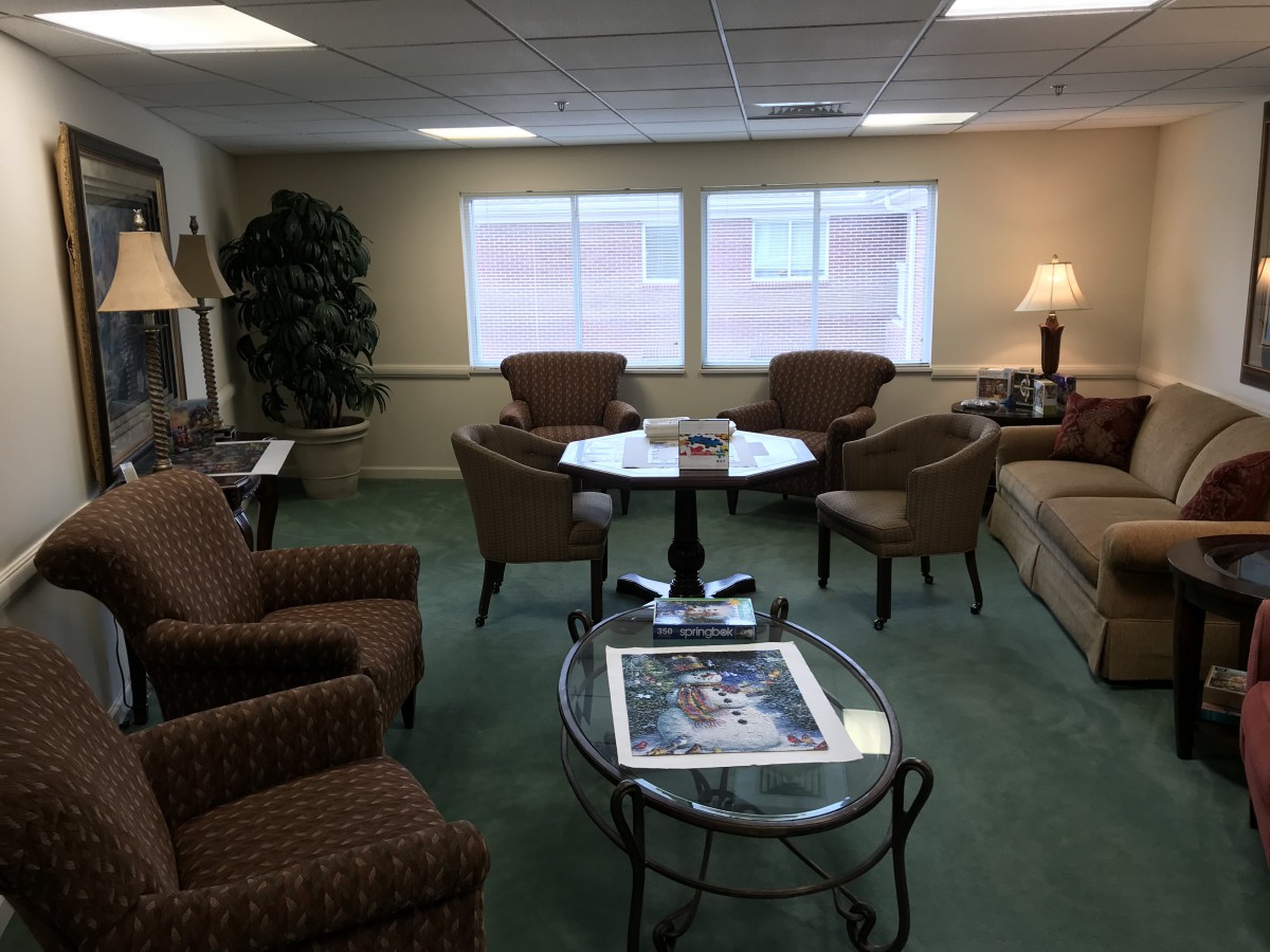 A cozy living room with sofas, chairs, and tables arranged neatly around a carpeted floor.