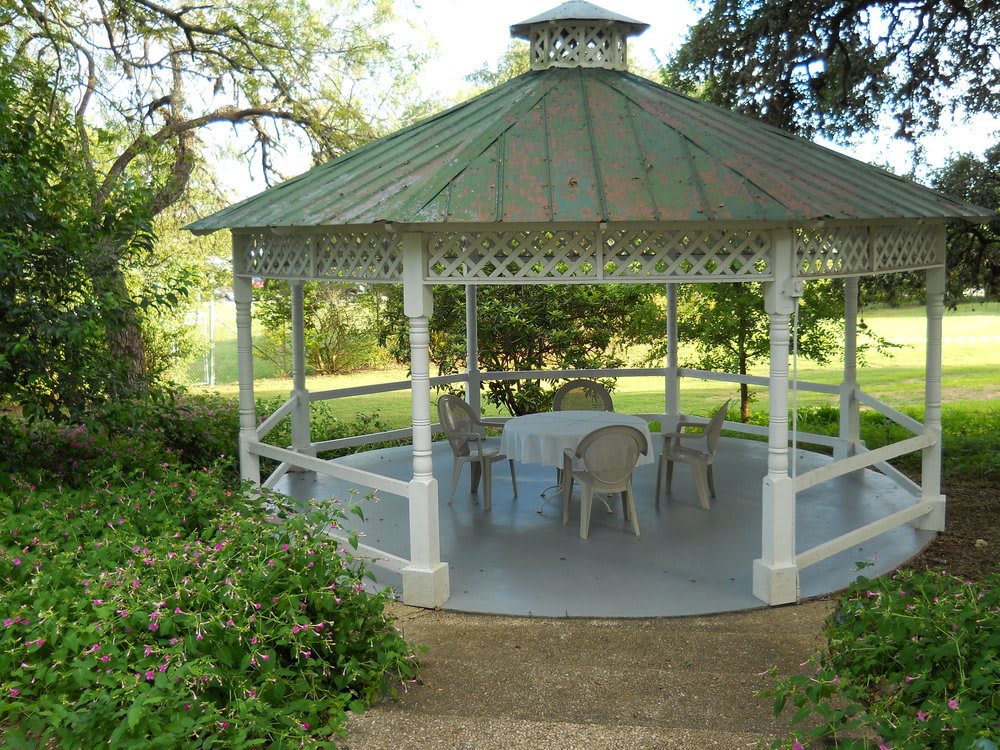 A charming outdoor gazebo surrounded by greenery, furnished with chairs and a table.