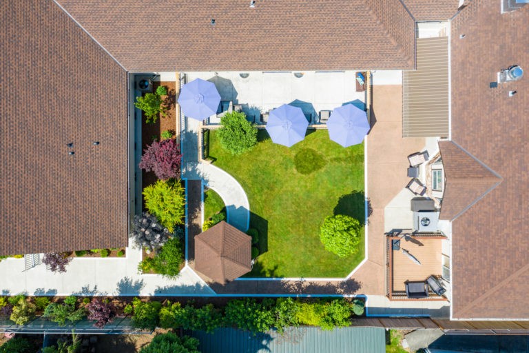 Aerial view of a well-landscaped backyard featuring a green lawn, patio with umbrellas, and garden areas.