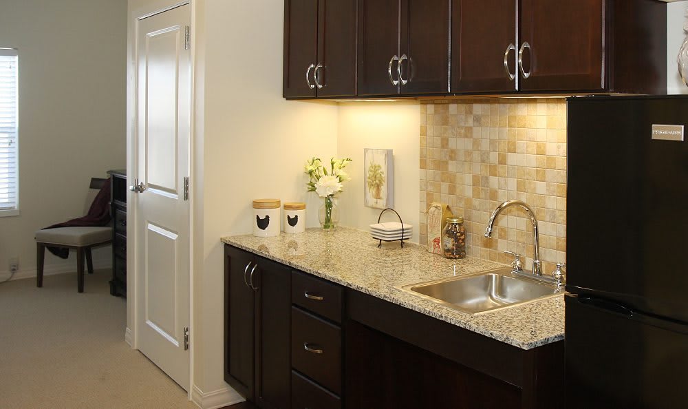 A modern kitchen features dark cabinets, a granite countertop with a sink, and elegant decor including a flower vase and small appliances.