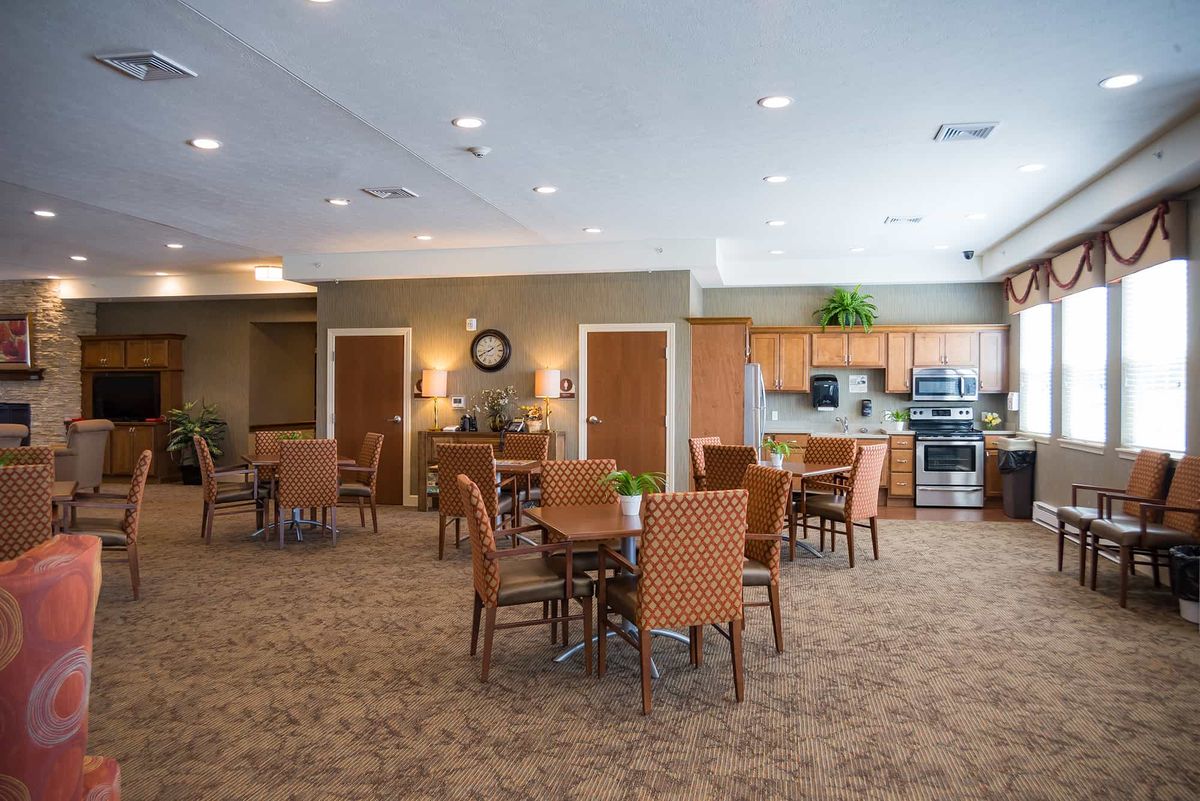 A spacious dining area with multiple tables and chairs, featuring a kitchen in the background.