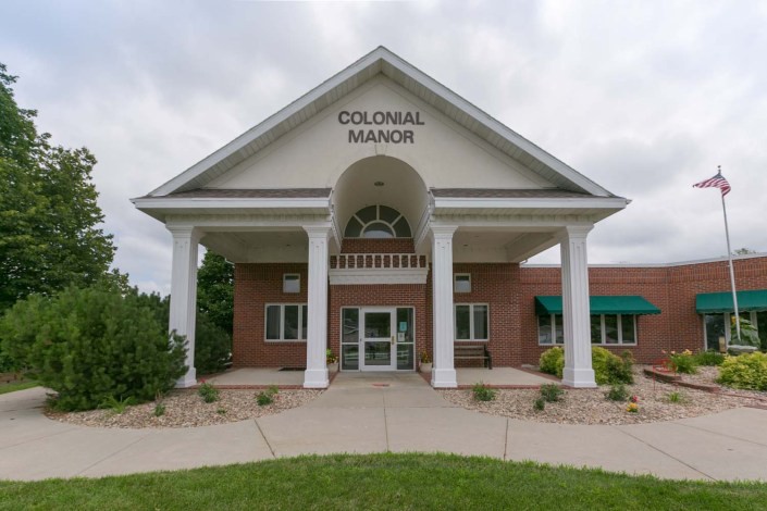 The entrance of Colonial Manor features a classic colonial architectural style with large columns and a welcoming pathway.