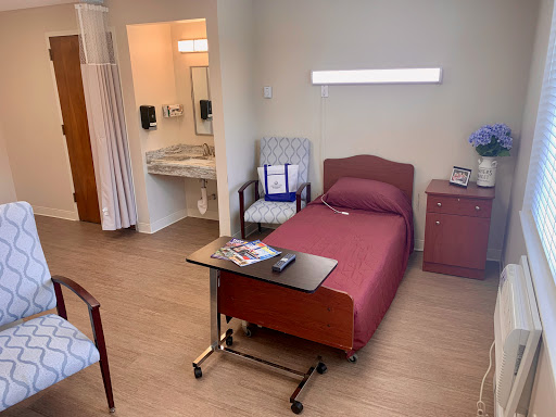 A view of a hospital patient room featuring a bed, chair, and attached bathroom.
