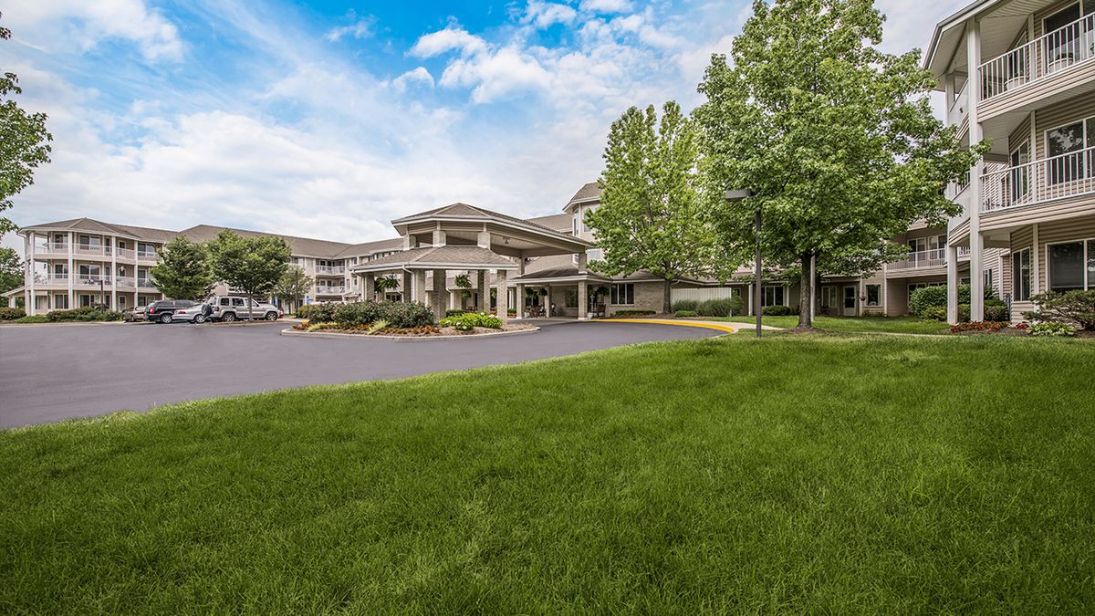 A modern building with a green lawn and trees under a blue sky with clouds.