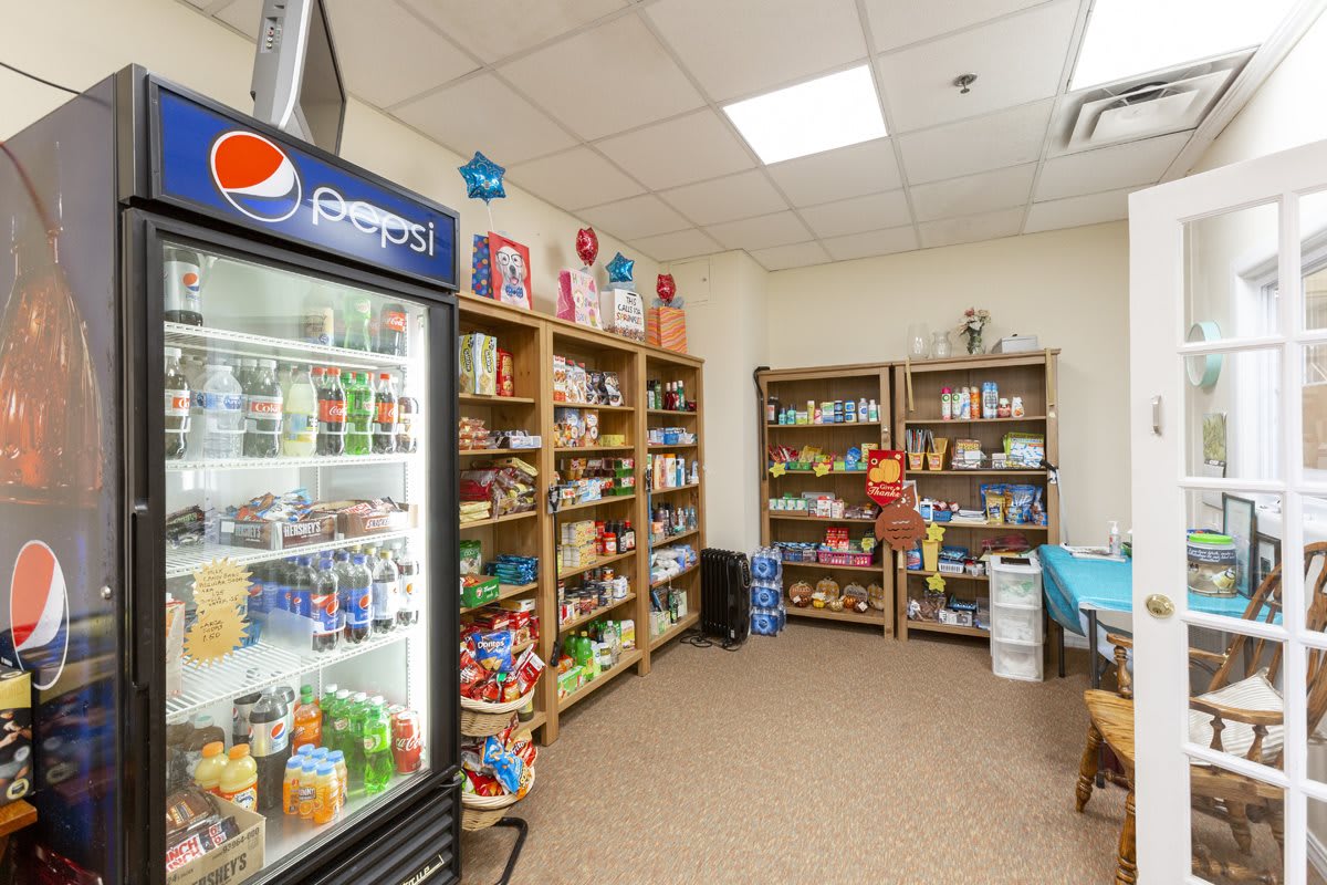 A small convenience store interior featuring shelves stocked with snacks and a refrigerator filled with drinks.