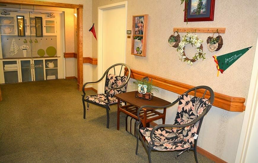 A cozy seating area in a hallway with decorative chairs, a small table, and wall decor including a wreath.