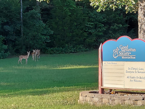 A serene scene featuring deer grazing in the grass near a welcoming sign.