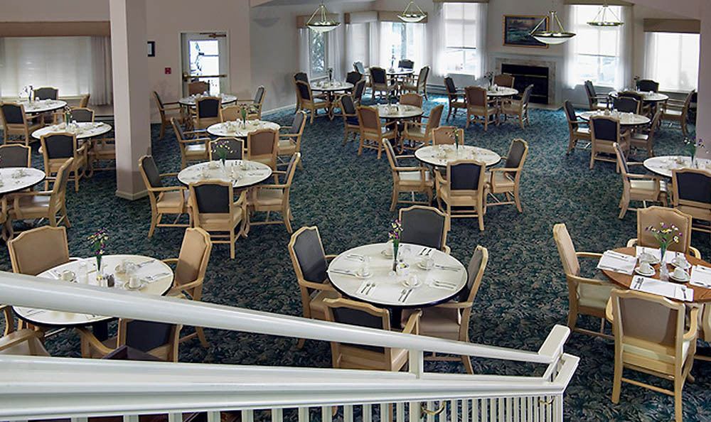 An empty dining area with round tables and chairs arranged neatly on a carpeted floor.