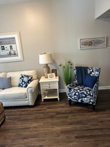 A cozy living room setup featuring a white sofa, a blue floral armchair, a lamp, and decorative elements.