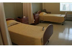 A hospital room featuring two beds with beige linens and wooden headboards.