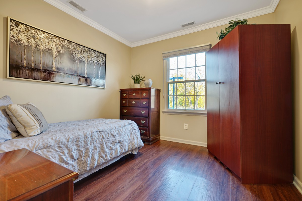 A cozy bedroom featuring a single bed, dresser, and wardrobe with natural light streaming through the window.