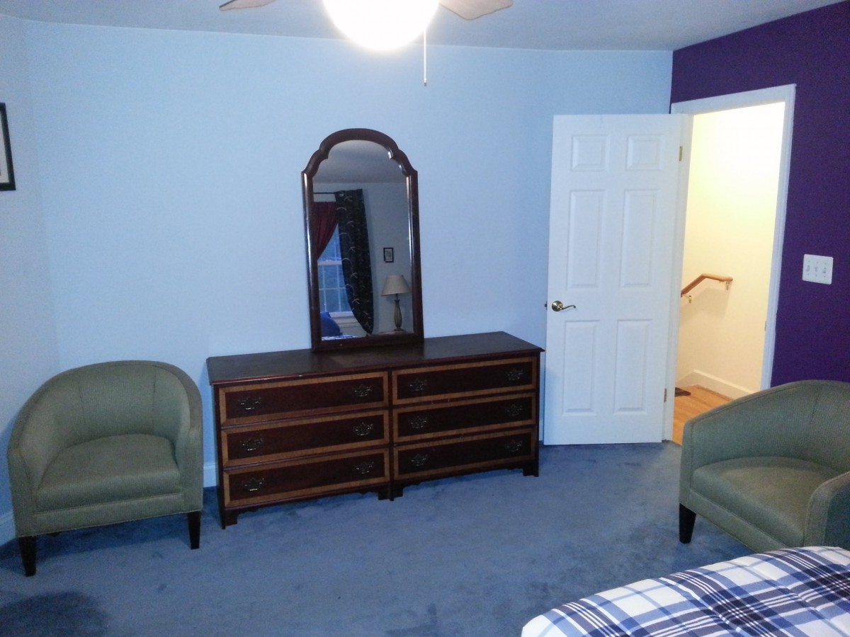 A bedroom with a dresser and mirror, two chairs, and blue walls.