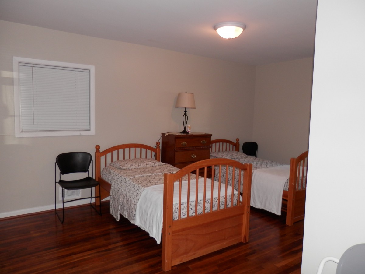 A minimalist bedroom with twin beds, a wooden dresser, and a chair.