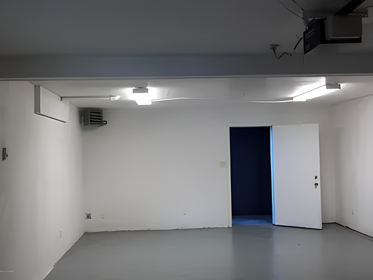 An empty room with white walls, an open door, and industrial lighting.