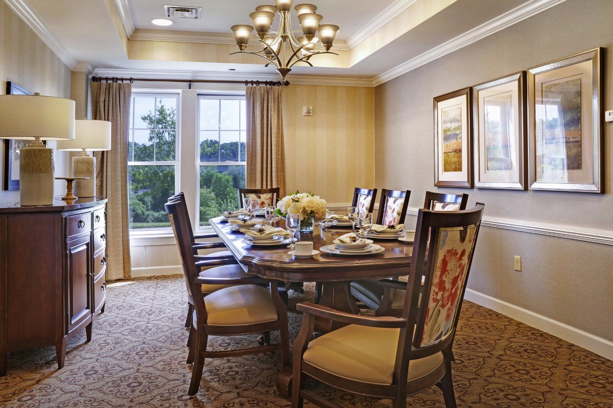 Elegant dining room with a large table set for dinner, featuring classic chairs, a chandelier, and large windows with curtains.