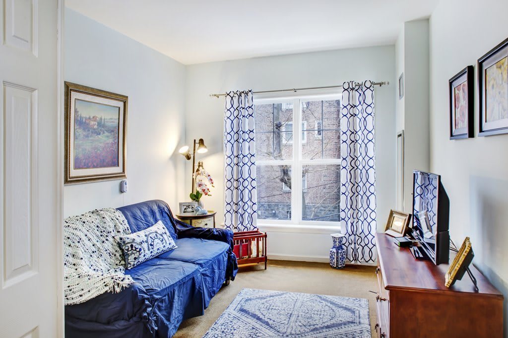 A cozy living room with a blue sofa, patterned curtains, and a television.