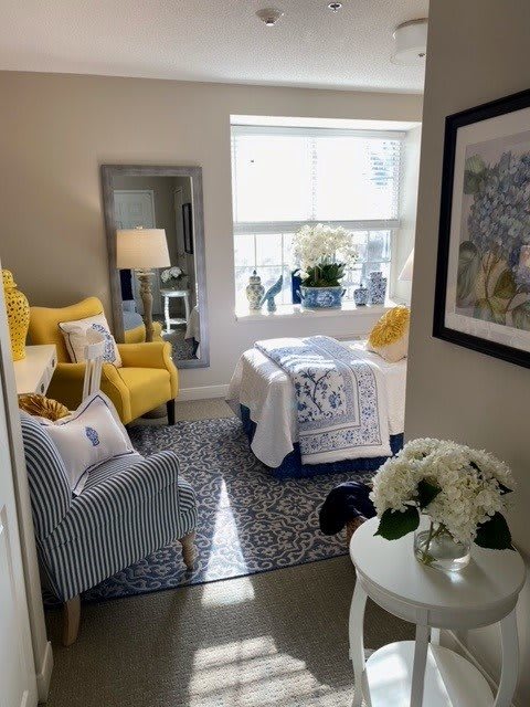 A cozy bedroom with bright yellow accents and a sunlit window, featuring a striped chair and a decorative floral arrangement.