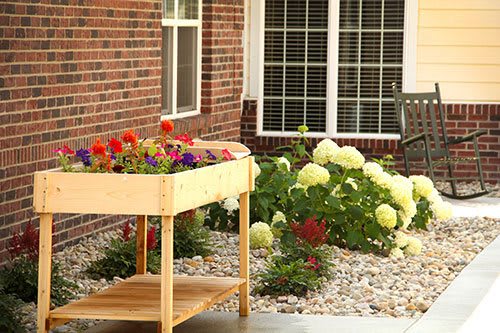 A charming garden with a wooden planter and vibrant flowers against a brick wall.